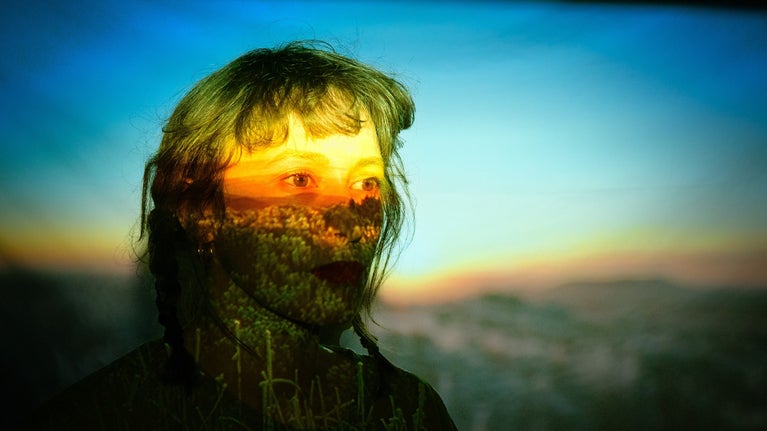 Woman's face with a landscape image projected across it.